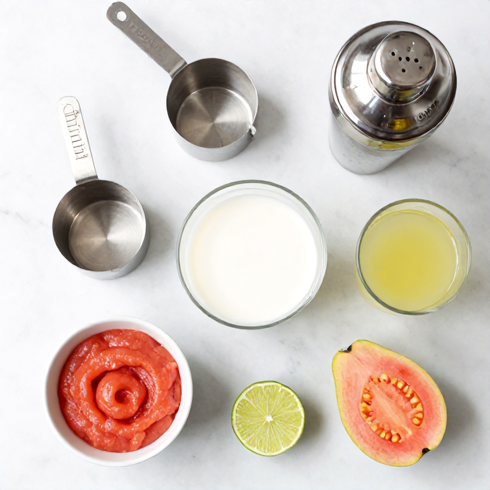 A flat lay of guava puree, coconut milk, lime juice, tequila, and triple sec. Measuring cups, a shaker, and a glass are visible.