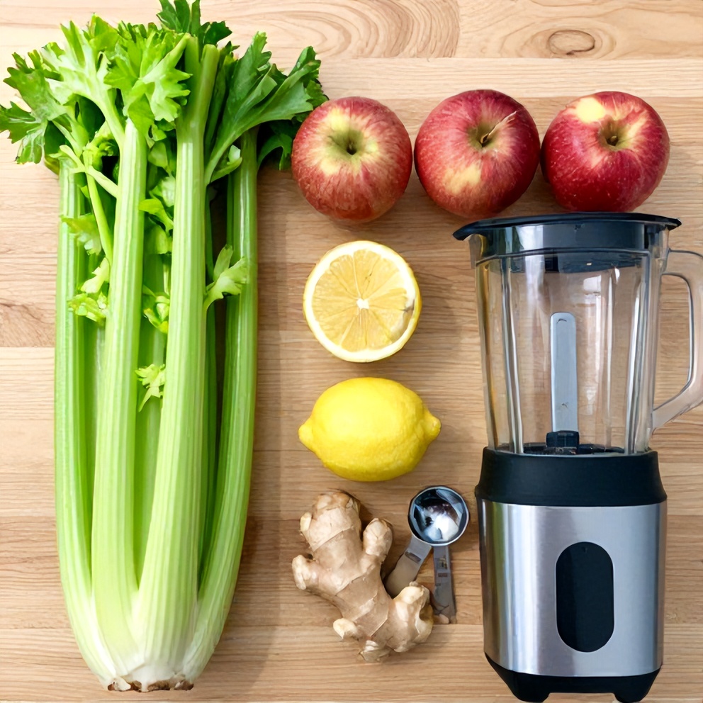 Celery, apples, lemon, ginger, and a blender on a wooden surface